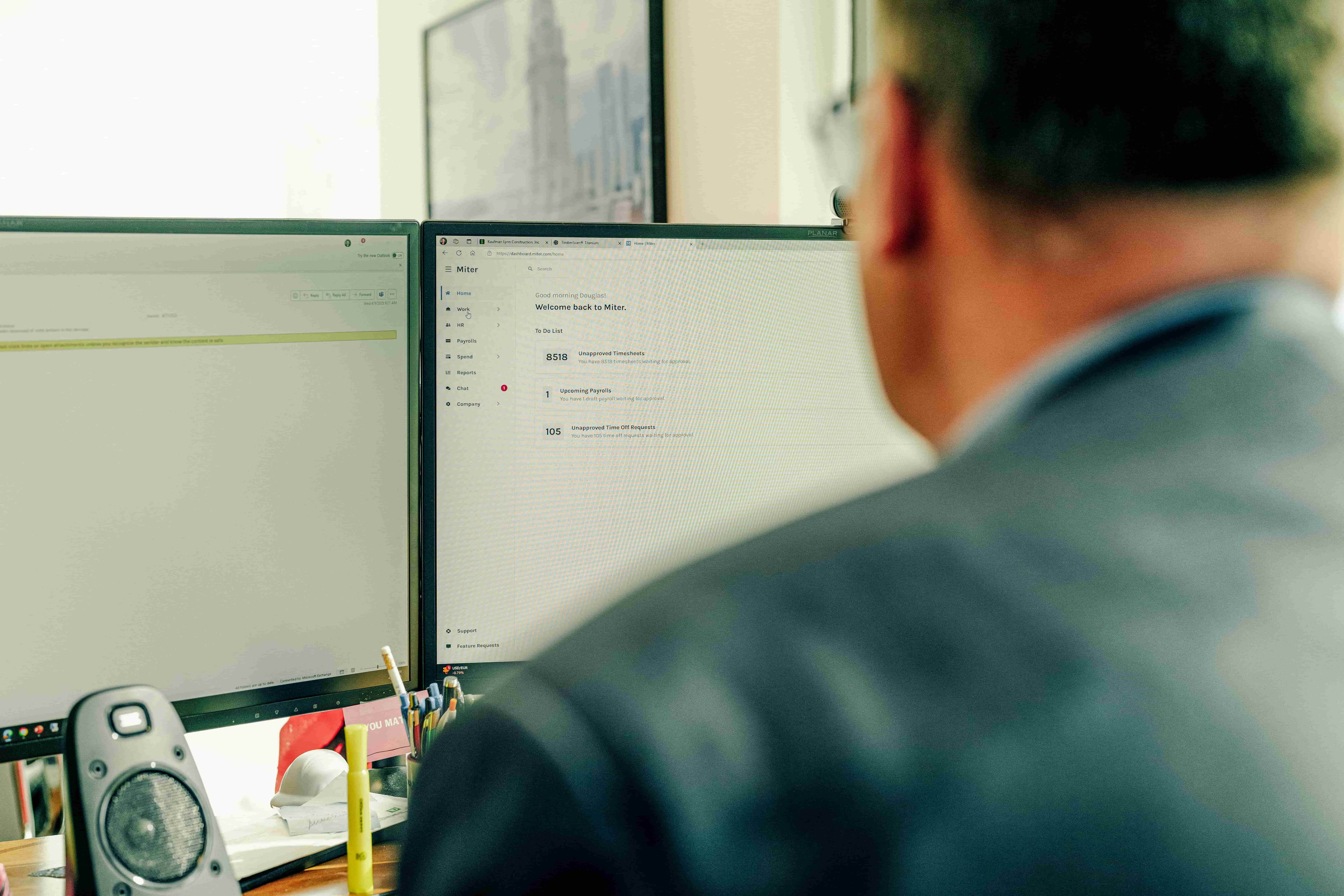 Man in black suit sitting at a desk reviewing union payroll on a computer screen.