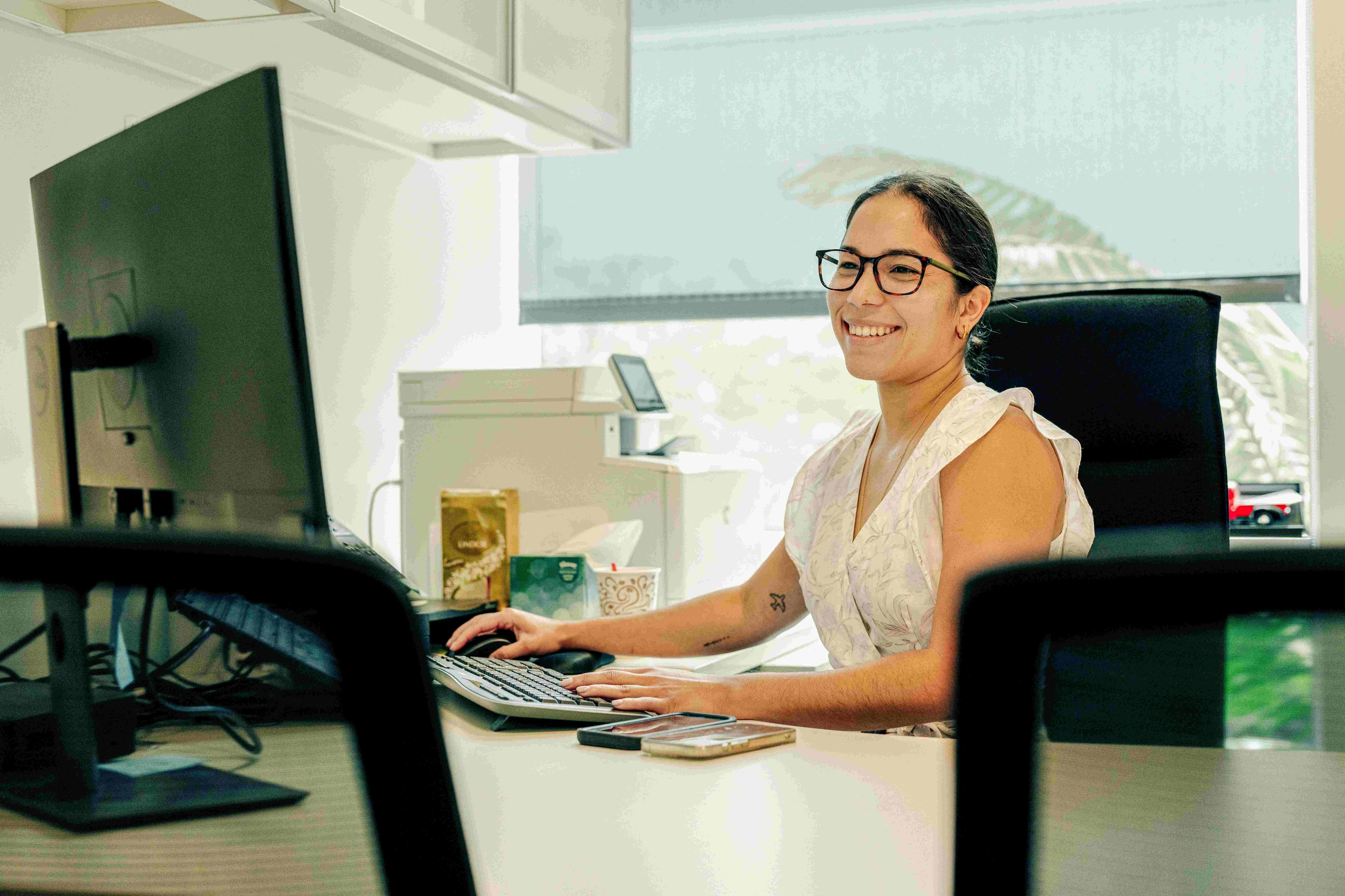 A women working at her desk on her computer smiling at the camera.