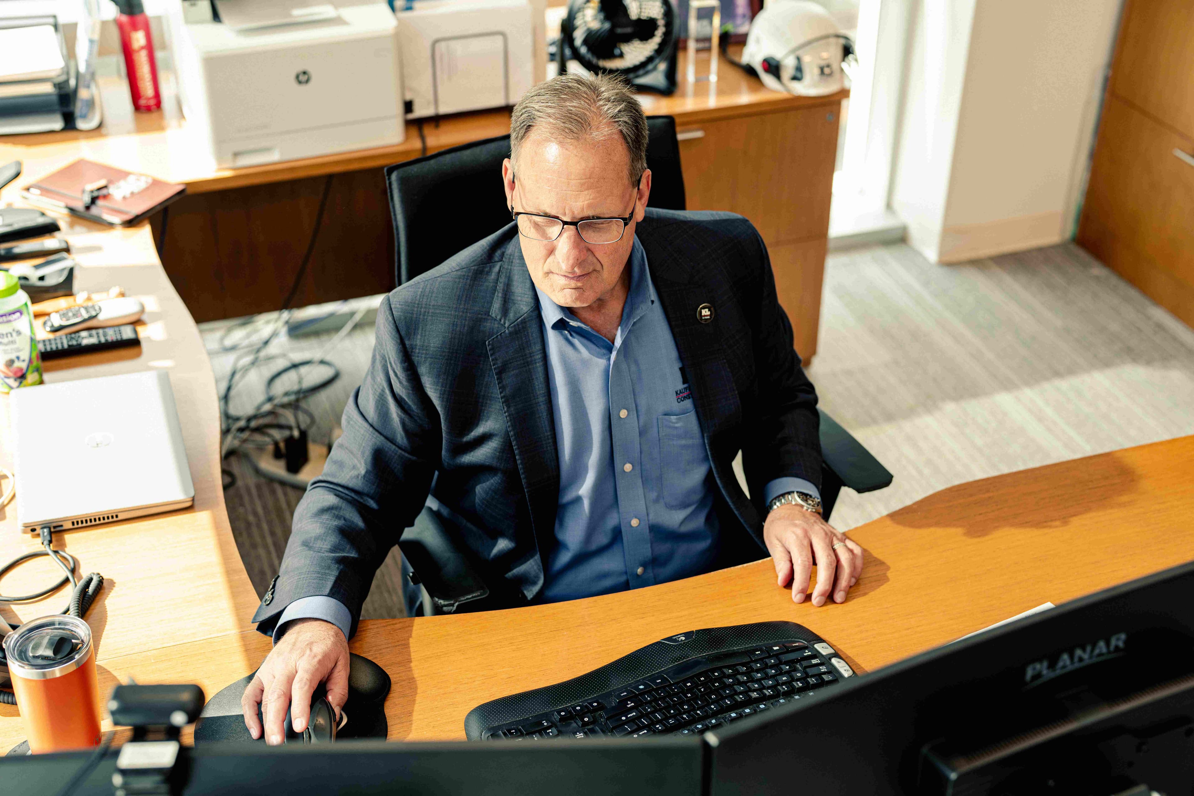 Man working in an office at his brown desk, using his mouse to navigate the contents of the screen.