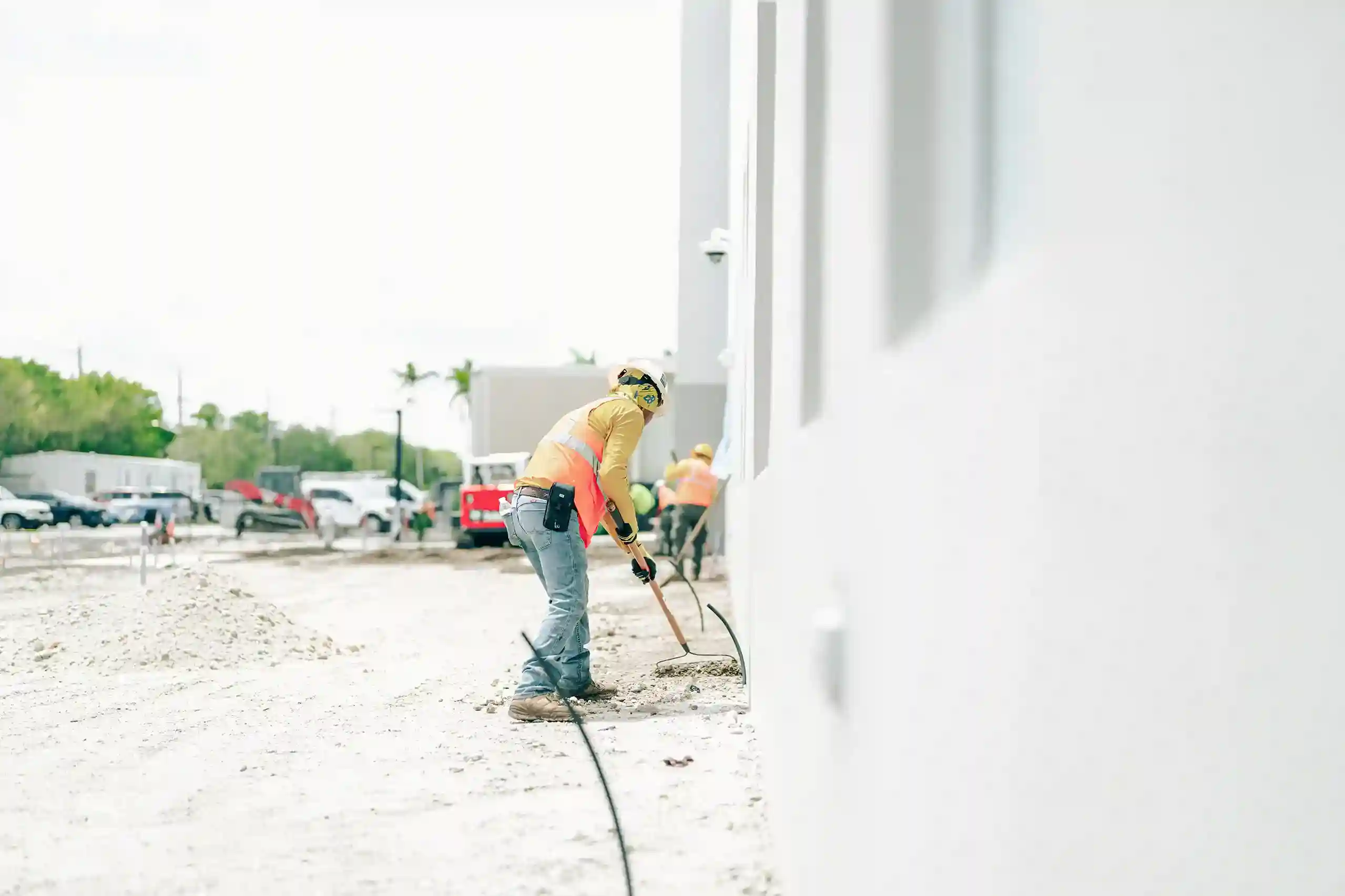 Construction field crew wearing a safety vest scaping ground close to a building
